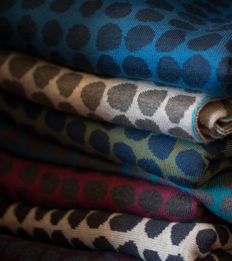 Stack of contemporary Scottish knitwear in abstract design of irregular dots. Blues, greys and red.