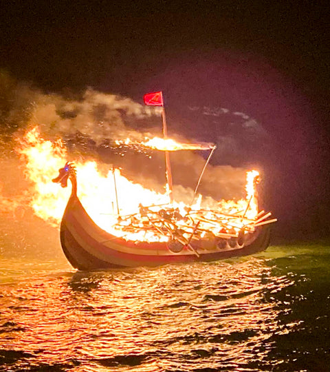 In the sea off Scousburgh Sands, Shetland, A replica viking galley is ablaze on the water. The masthead is a dragon