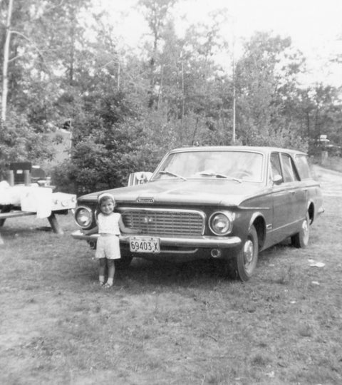 Black and white photograph of young Niela, standing in front of a car