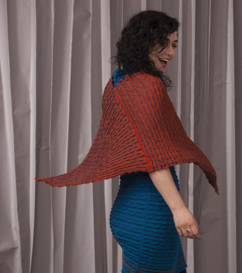 A girl wears a blue dress with an orange knitted cape over. She spins so that the cape flies out.