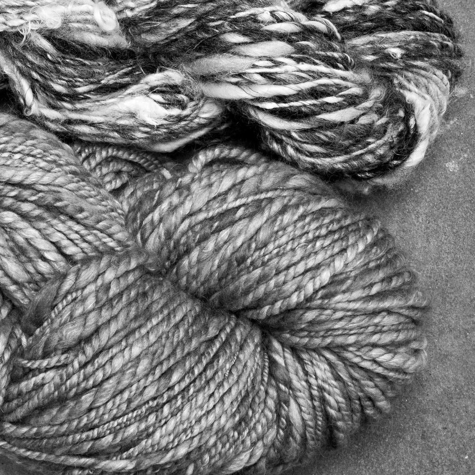 two skeins of hand-spun art yarn. the top one is bulky and freely spun, with the bottom being finer and with a sheen. Both are two ply