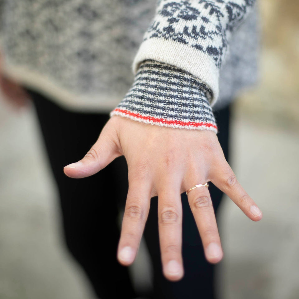 detail of an inset storm cuff on the shetland fair isle smookie jumper. the cuff is striped in charcoal and off white, with a red stripe.