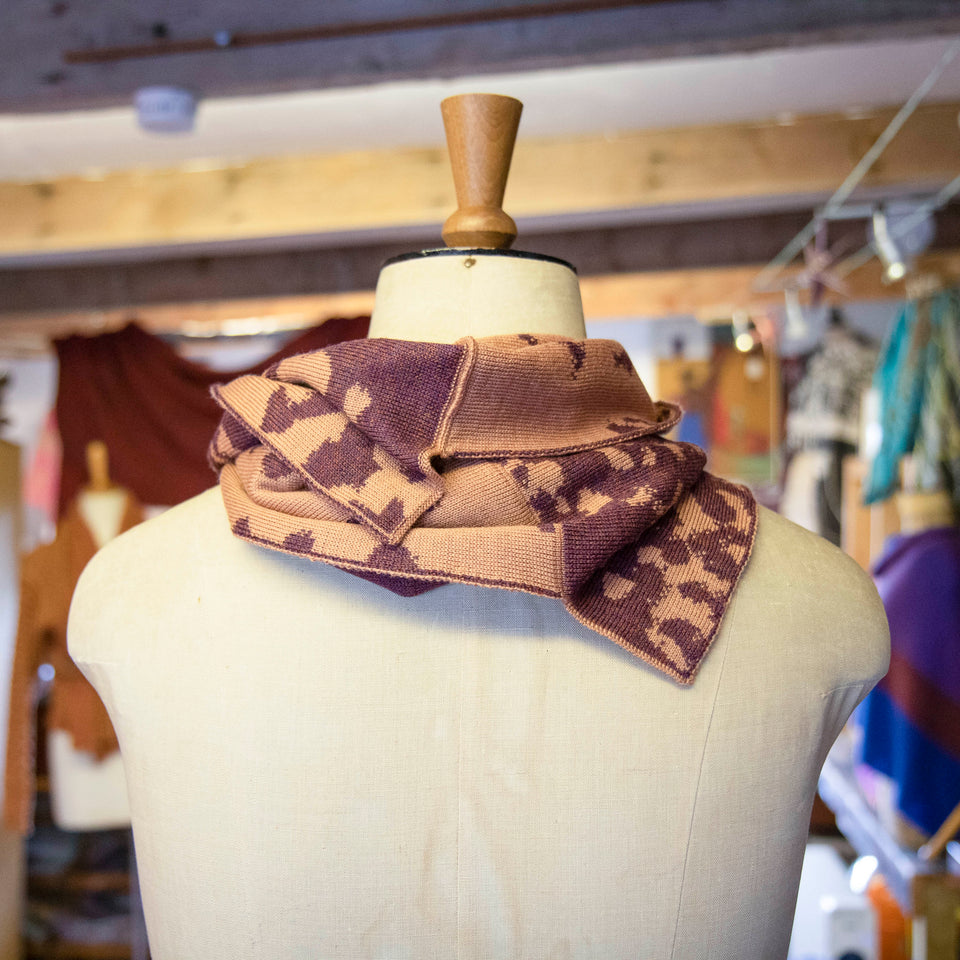 Asymmetric circle scarf in salmon and soft aubergine, in a mottled pattern on a mannequin in the Nielanell knitwear studio, Shetland.