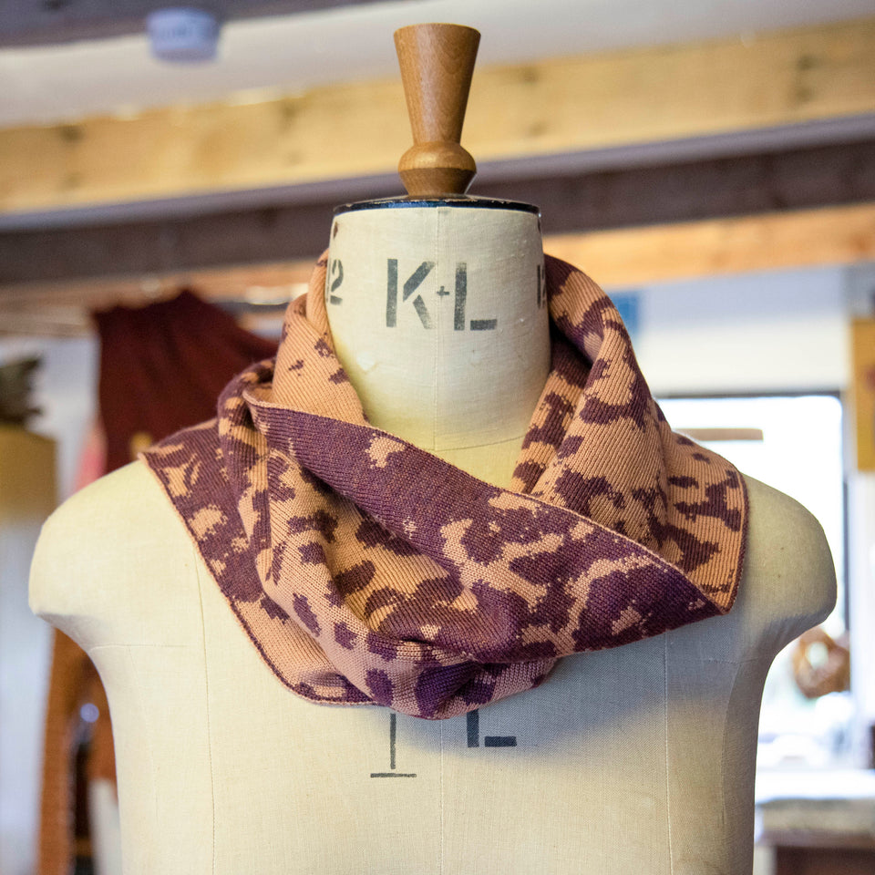 Asymmetric circle scarf in salmon and soft aubergine, in a mottled pattern on a mannequin in the Nielanell knitwear studio, Shetland.