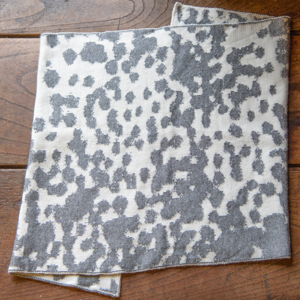 a finely knitted circular scarf with asymmetric seam in a mottled pattern - steel grey and off white - laid flat on wooden floor.