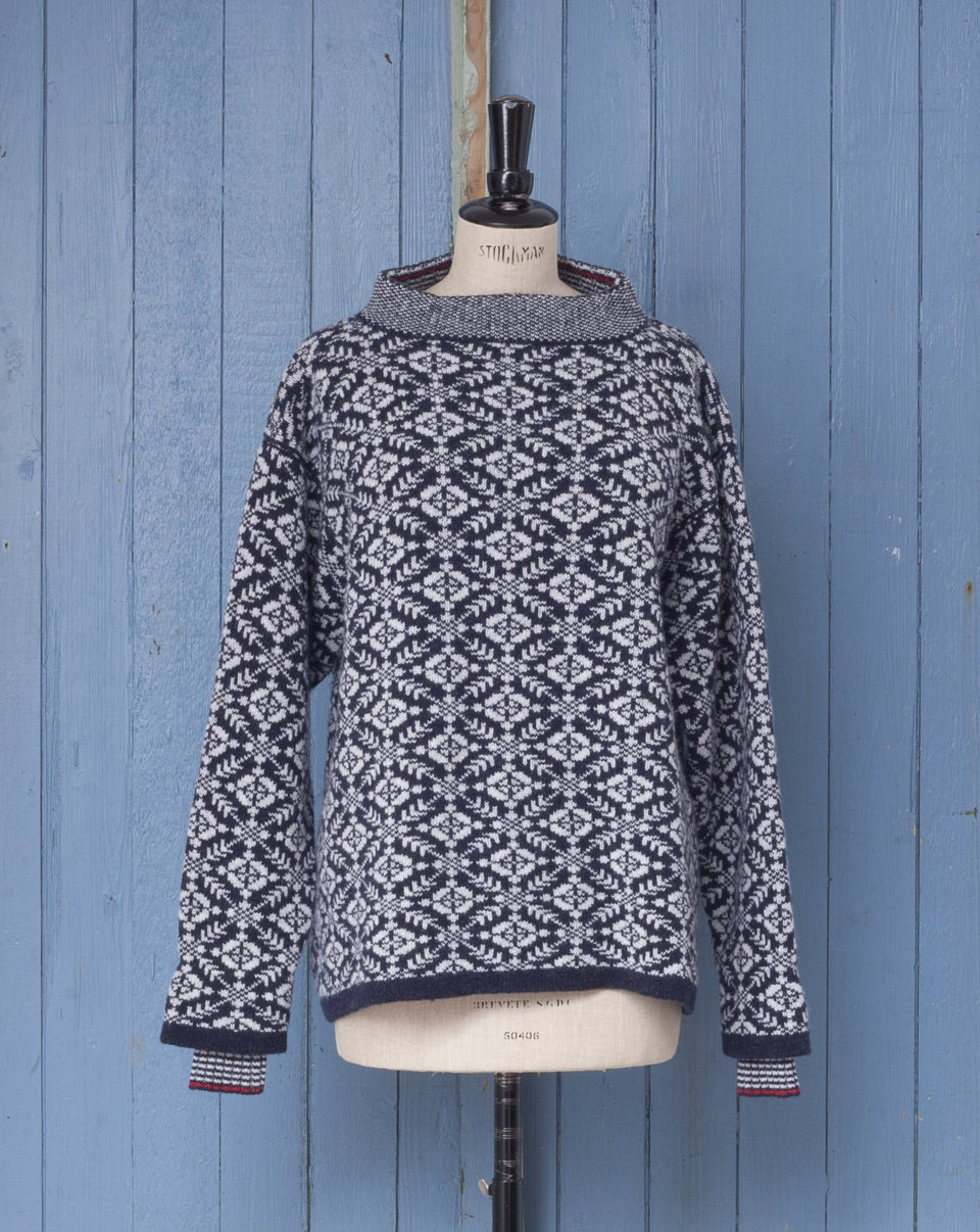Fair Isle jumper, front view. Modern design with all-over nordic inspired pattern, striped inset cuff and stand up neck. Shown in navy and white with dark scarlet trim