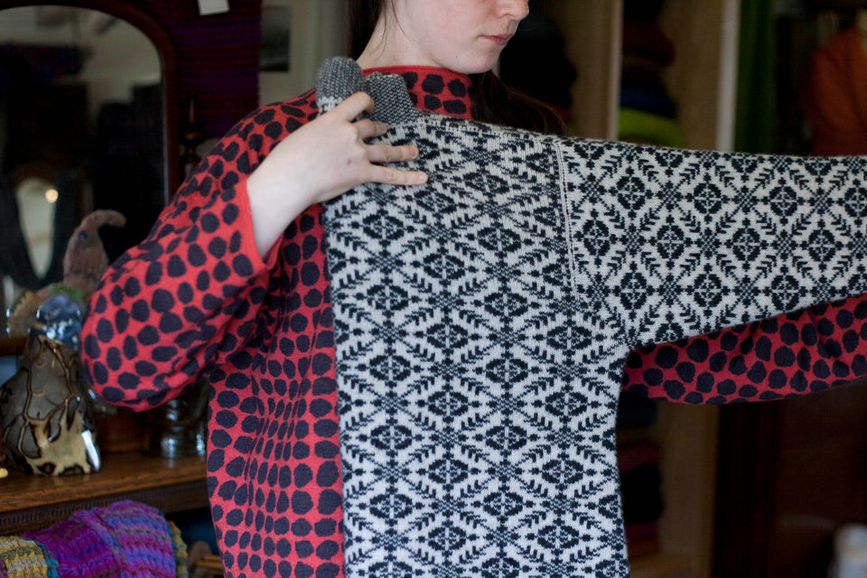 Shetland Smookie Fair Isle jumper. All over pattern with striped inset cuff and stand up neck. Shown in dark navy and white, being folded by an assistant at the Nielanell studio in Shetland.