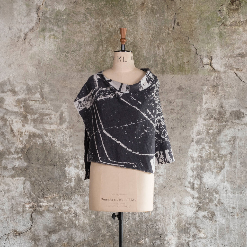Knitted Byre capelet. Abstract, graphic design in an asymmetric shape. Shown in Charcoal and stone white. Front view on mannequin