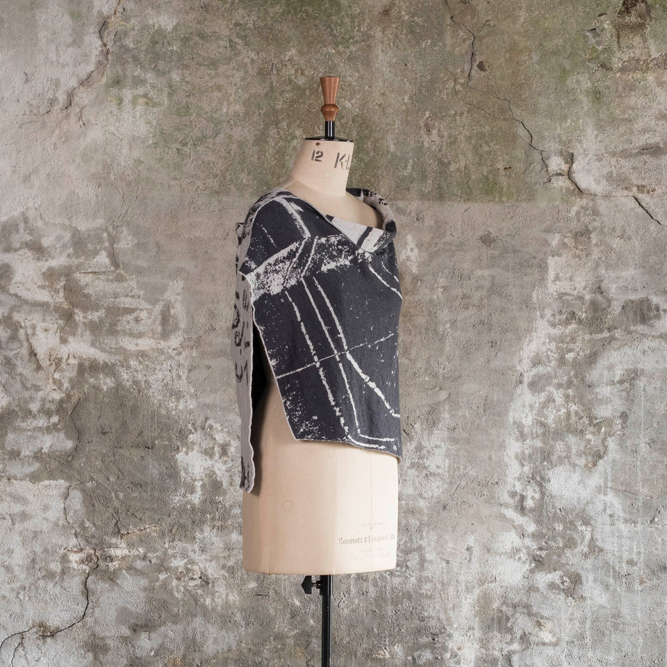 Knitted Byre capelet. Abstract, graphic design in an asymmetric shape. Shown in Charcoal and stone white. 3/4 side view on mannequin, showing side opening