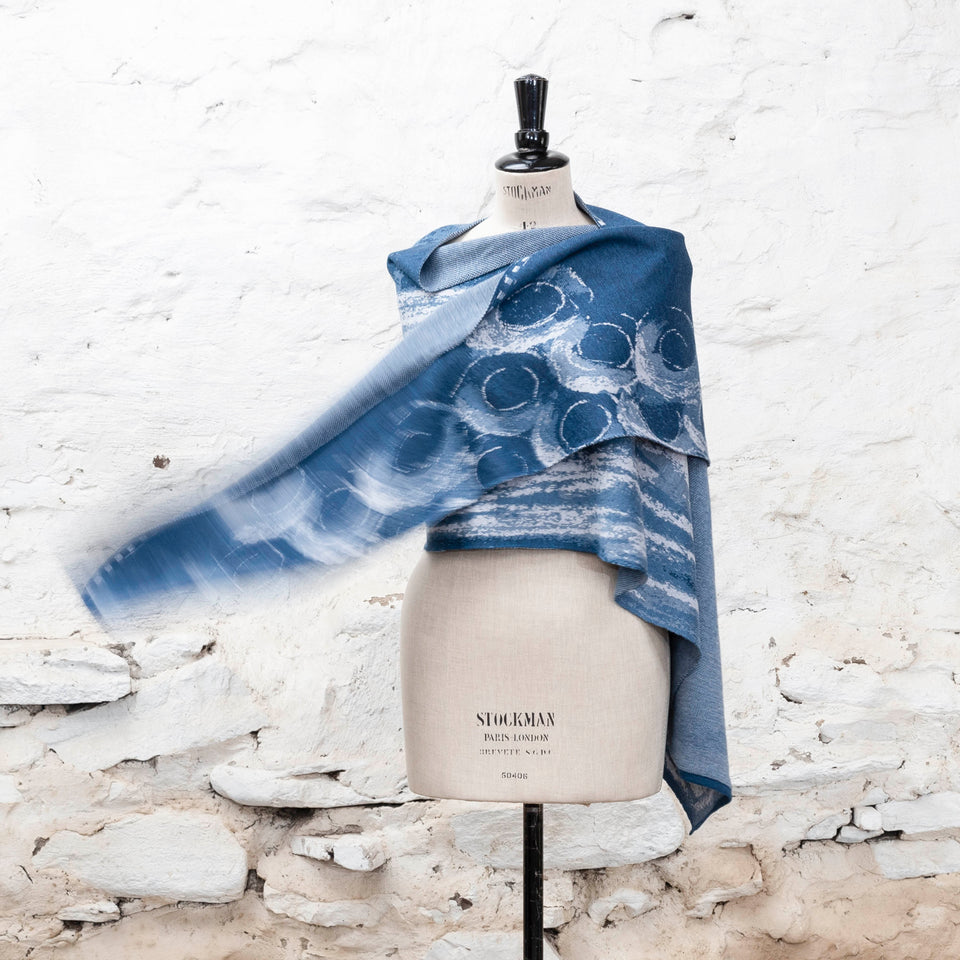 Finely knitted shawl in luxurious merino, made in Scotland. Shown on a vintage mannequin against a whitewashed wall. Abstract design in sea blues with curvilinear motifs