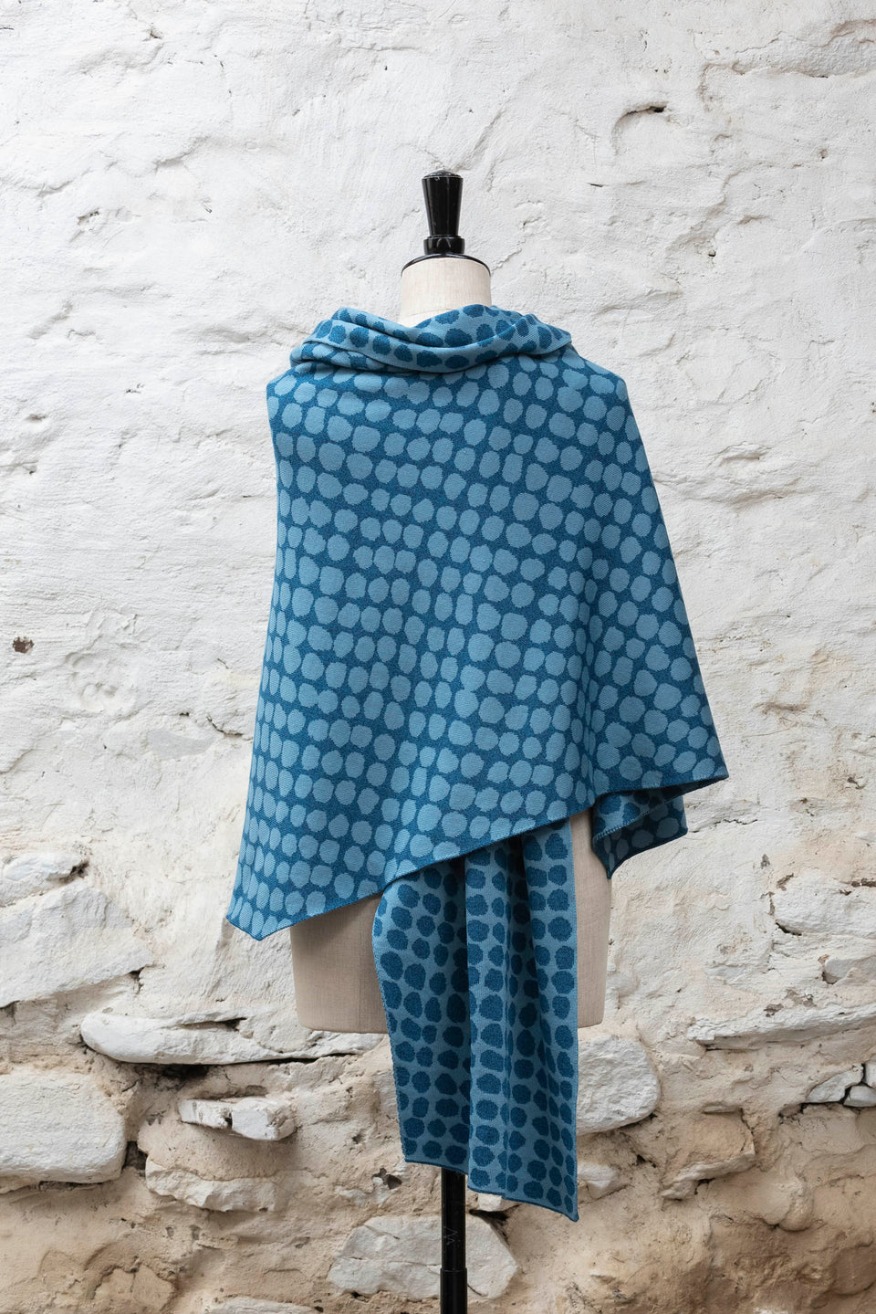 Knitted ebb-stanes wrap with irregular dot pattern shown in blues