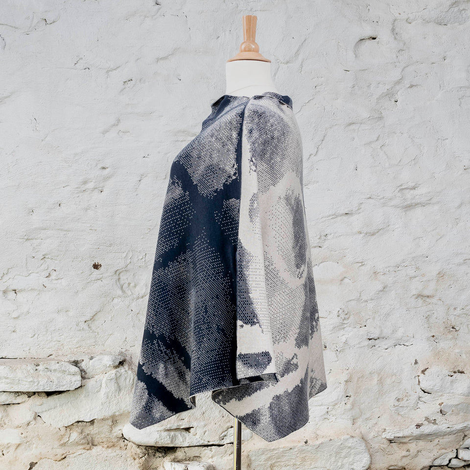Knitted Rani cape. Small abstract patterns make up a larger design with photographic imagery. Shown in inky blue and antique white