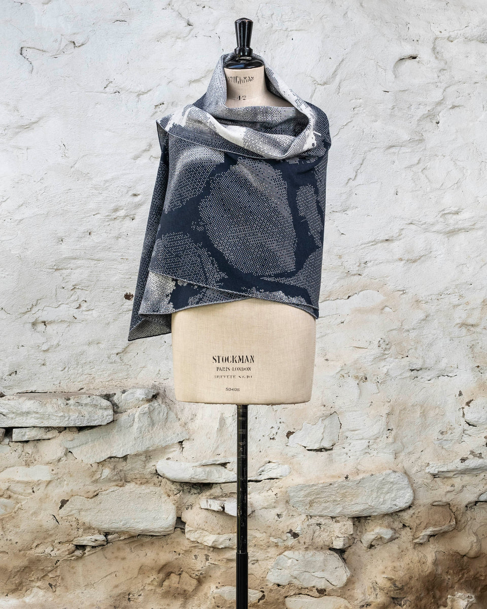 Knitted Rani shawl / wrap. Small abstract patterns make up a larger design with photographic imagery. Shown in inky blue and antique white