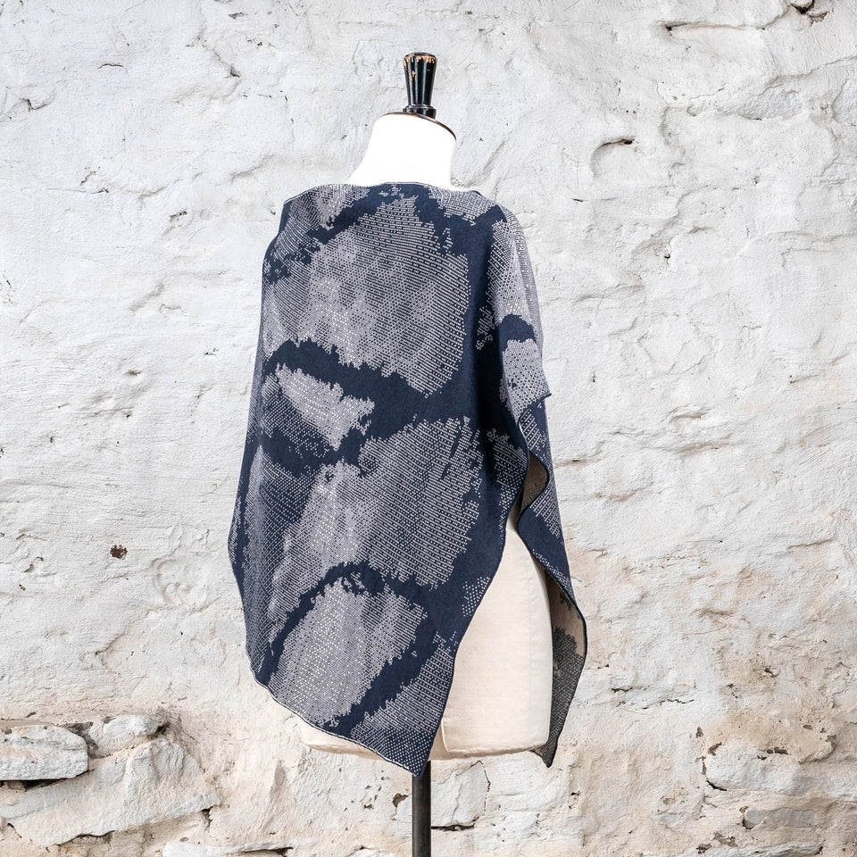 Knitted Rani shorter cape. Small abstract patterns make up a larger design with photographic imagery. Shown in inky blue and antique white