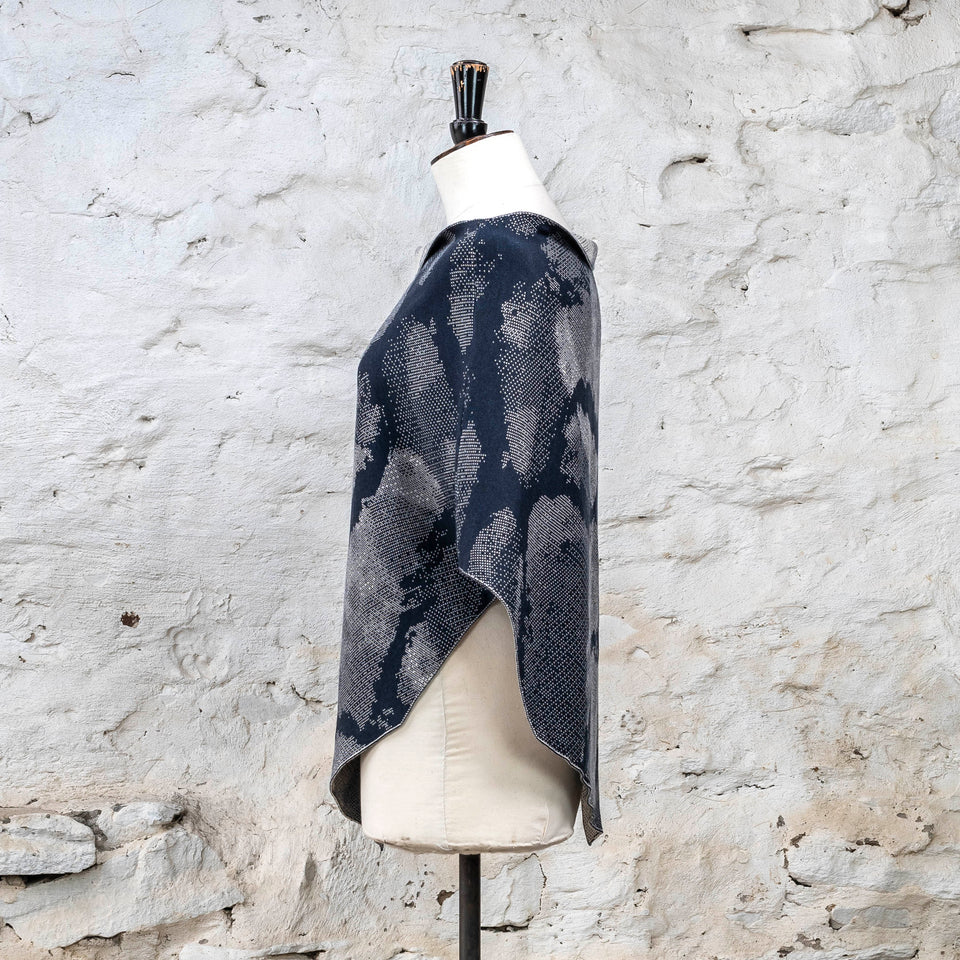 Knitted Rani shorter cape. Small abstract patterns make up a larger design with photographic imagery. Shown in inky blue and antique white
