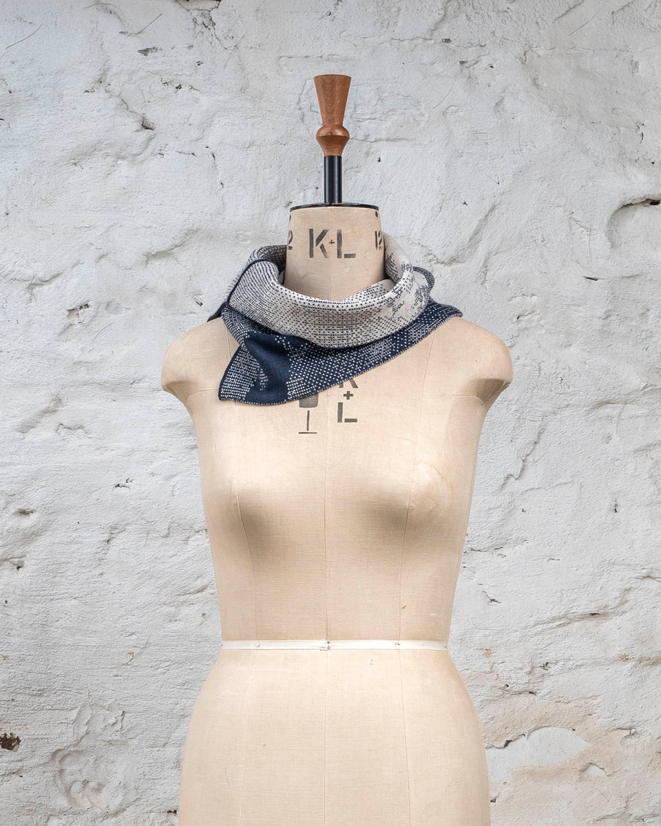 Knitted Rani asymmetric cowl. Small abstract patterns make up a larger design with photographic imagery. Shown in inky blue and antique white