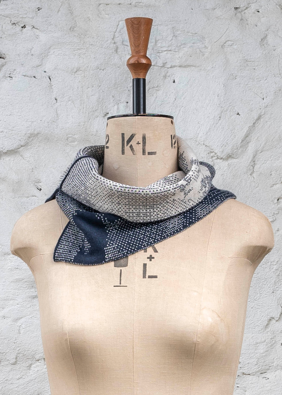 Knitted Rani asymmetric cowl. Small abstract patterns make up a larger design with photographic imagery. Shown in inky blue and antique white