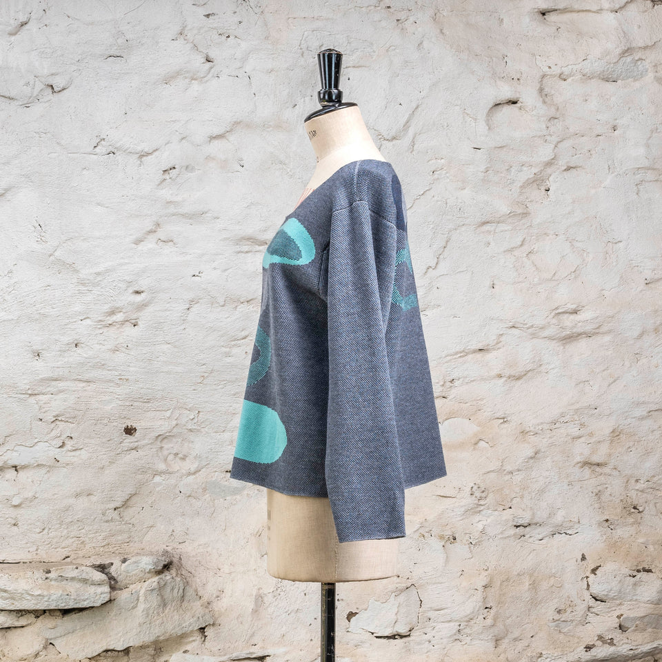 Side view from left of knitted 'conversation pieces' contemporary jumper in blues with accents in aqua. The pattern is abstract