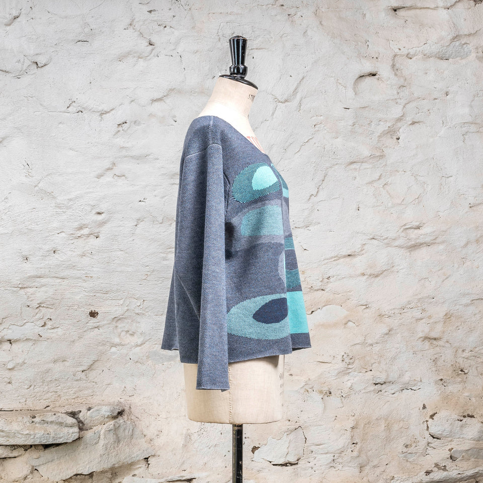 Side view from right of knitted 'conversation pieces' contemporary jumper in blues with accents in aqua. The pattern is abstract