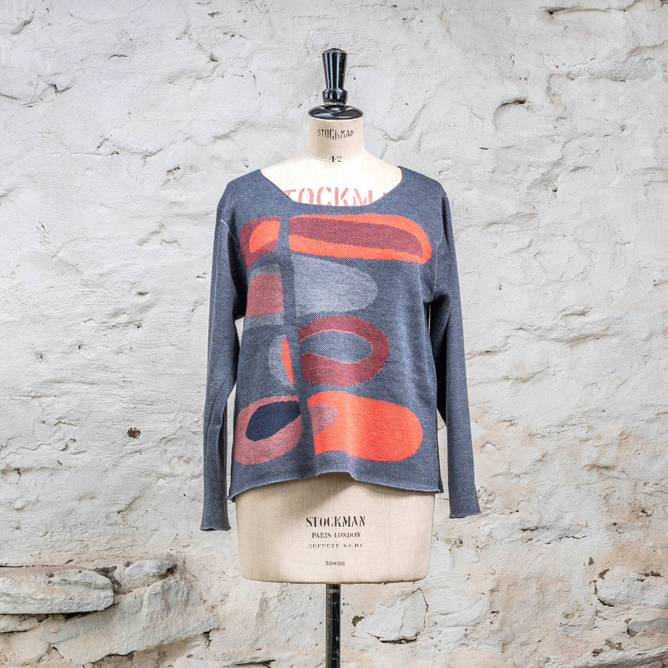 Seen from the front, contemporary Scottish knitted jumper with gently scooped neck. In blues with accents in coral. The pattern is abstract