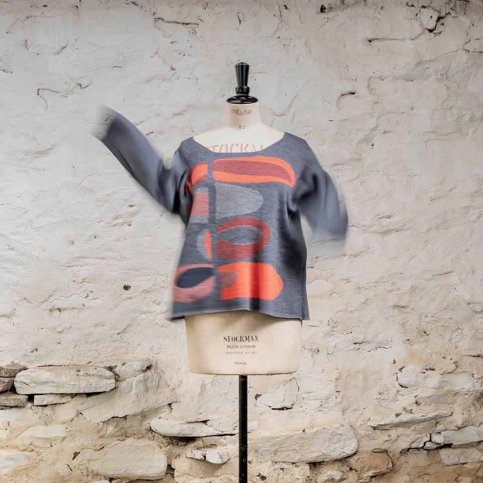 Front view, with moving arms, of knitted contemporary Scottish jumper in blues with accents in coral. The pattern is abstract