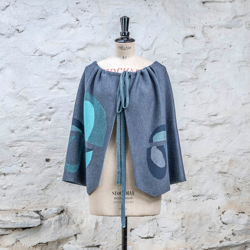 Knitted wrap skirt in blues with accents in aqua, worn as a cape. The pattern is abstract. 