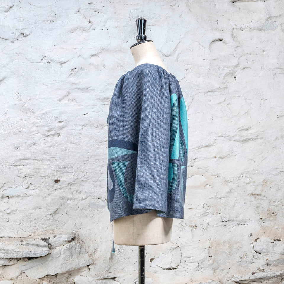 Knitted wrap skirt in blues with accents in aqua, worn as a cape. The pattern is abstract. 