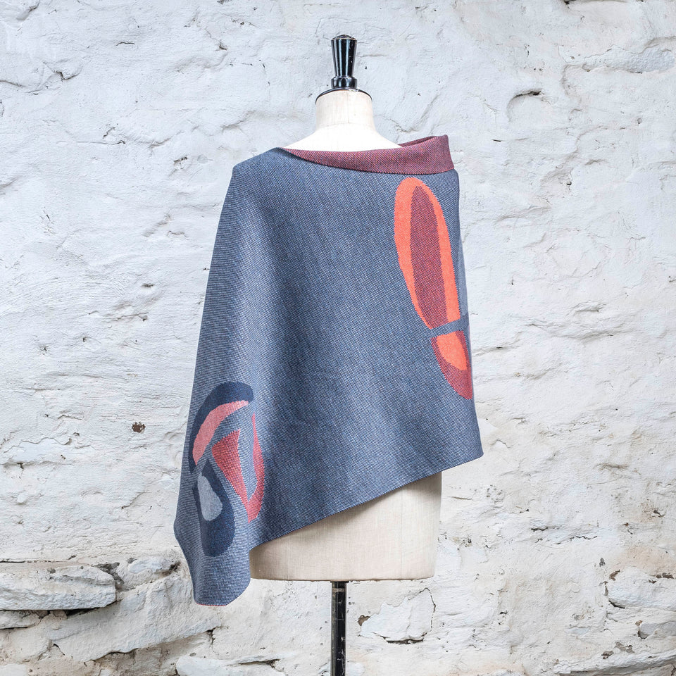 Knitted cape in blues with accents in coral. The pattern is abstract