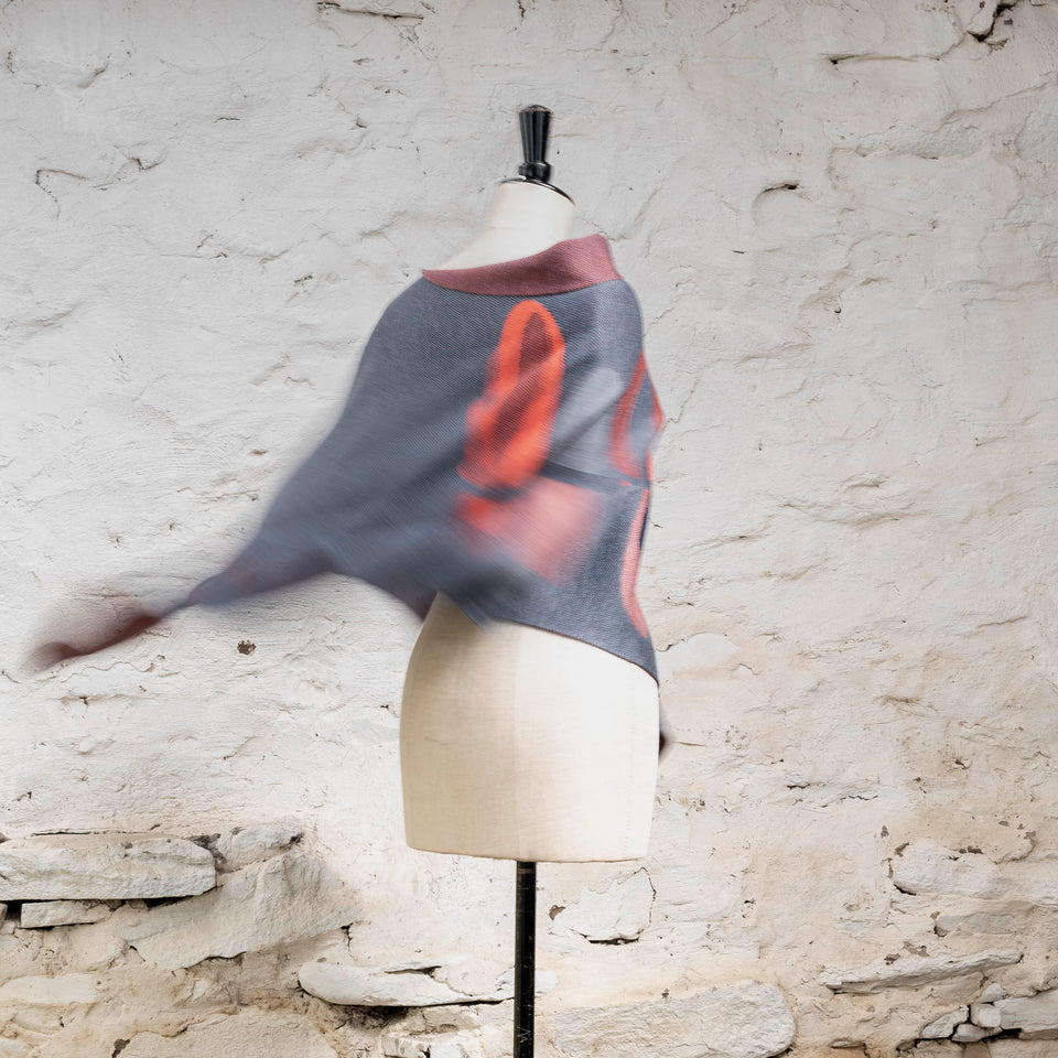 Knitted cape in blues with accents in coral. The pattern is abstract