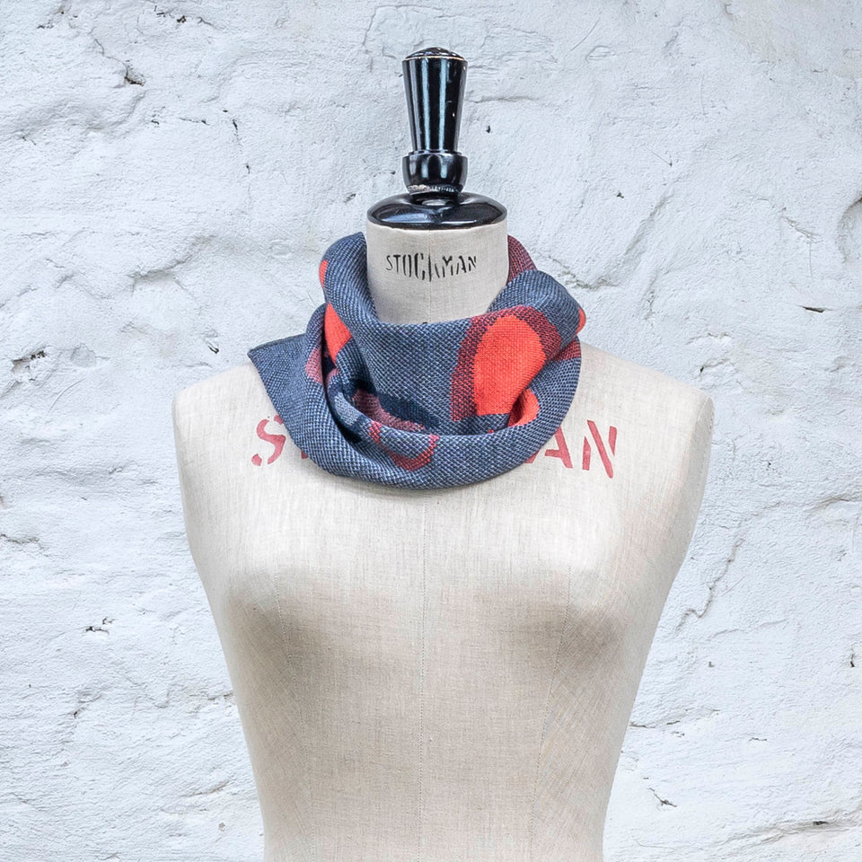 Knitted cowl in blues with accents in coral. The pattern is abstract