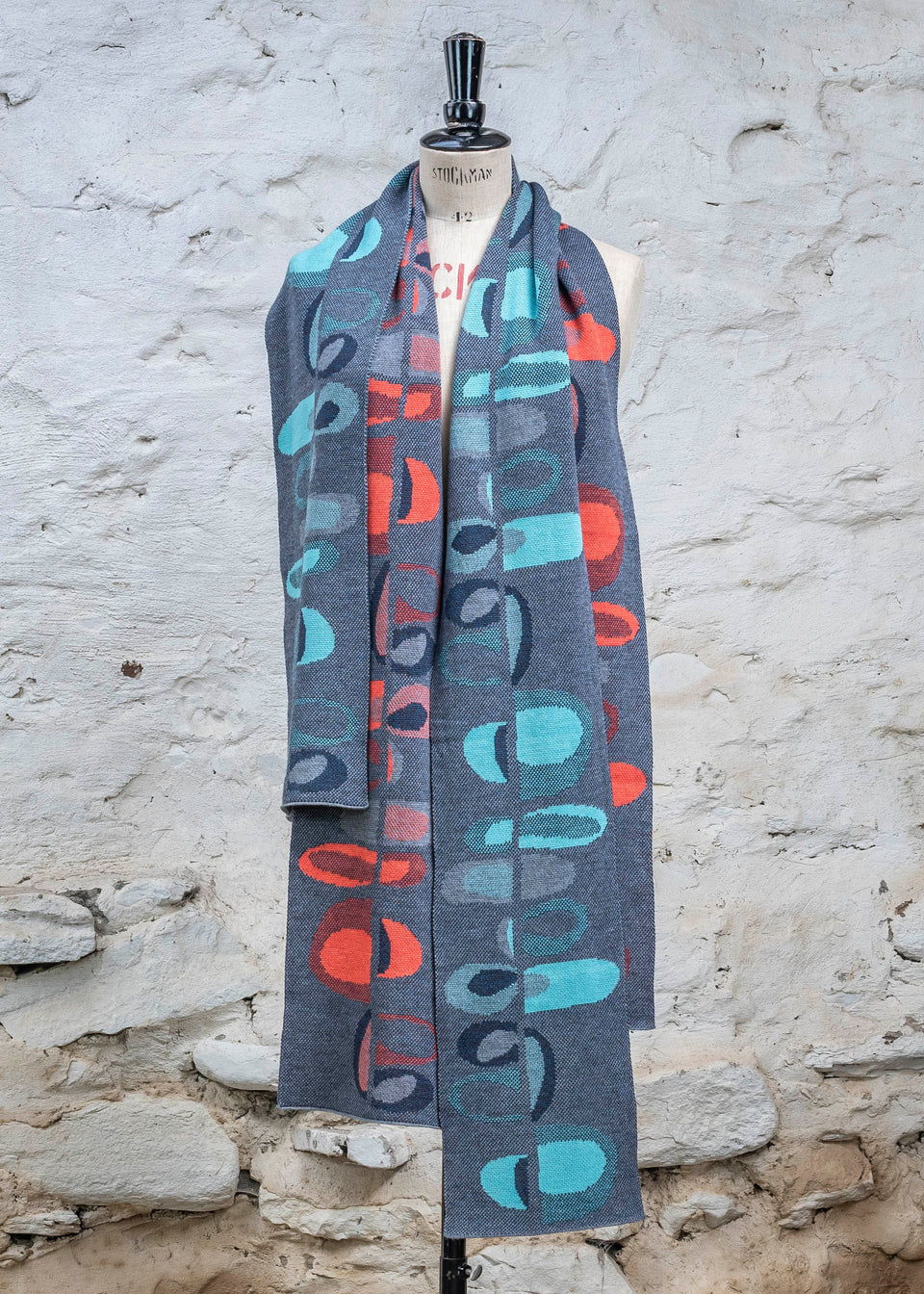 Knitted scarf in blues with accents in aqua or coral. The pattern is abstract