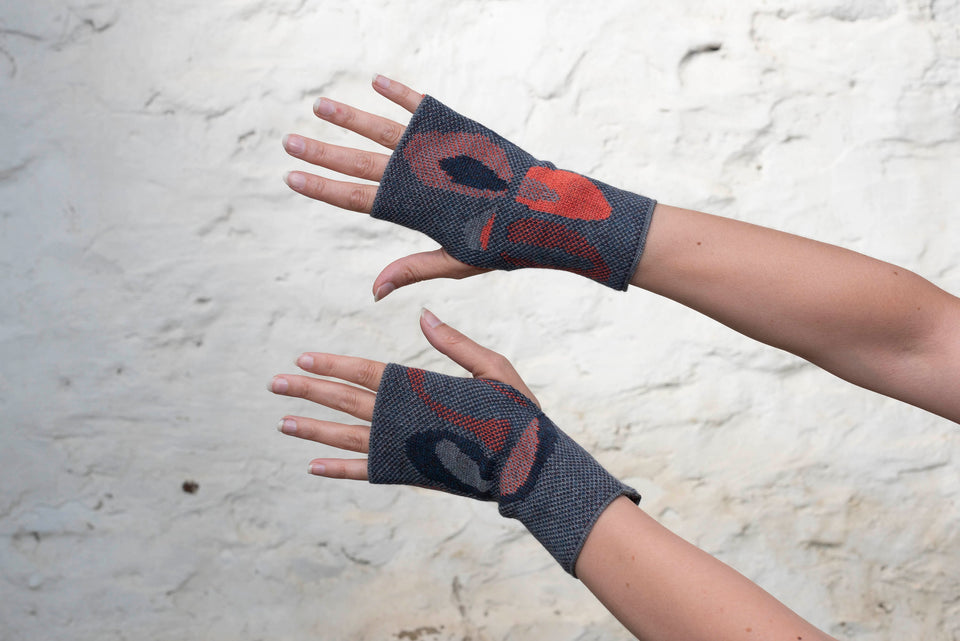 Knitted gauntlet mitts in blues with accents in coral. The pattern is abstract