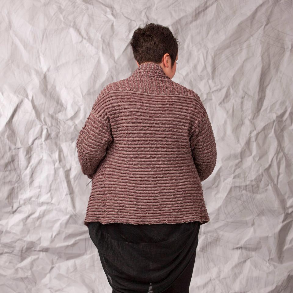 Model wears a longline knitted contemporary jacked in ridged fabric, in warm beige and cherry. Back view showing higher neck at back