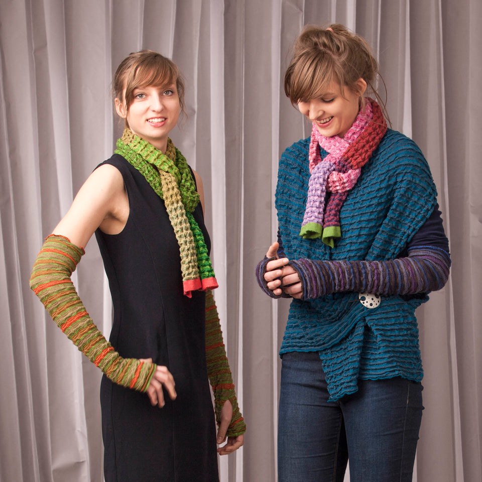 Models wear rigg scarves. The rigg textile is ridged and knitted in coloured stripes. Scarves have blocks of colour running through the length