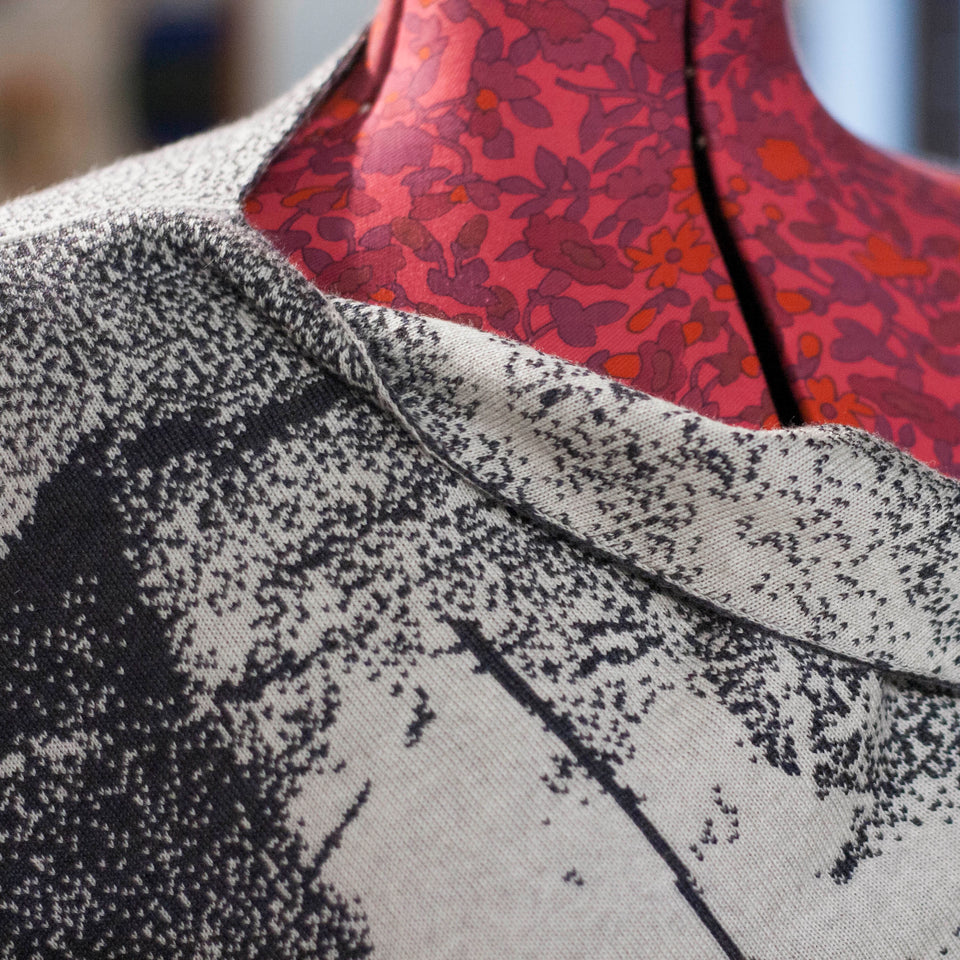 Knitted Byre cape. Abstract, graphic design in an asymmetric shape. Shown in Charcoal and stone white. Detail of neckline