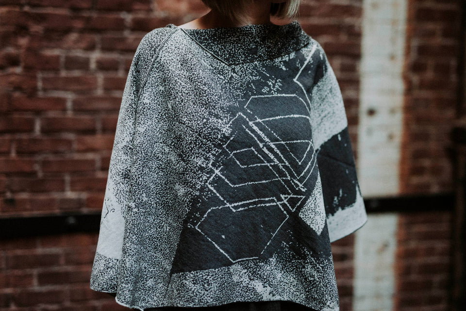 Knitted Byre cape. Abstract, graphic design in an asymmetric shape. Shown in Charcoal and stone white