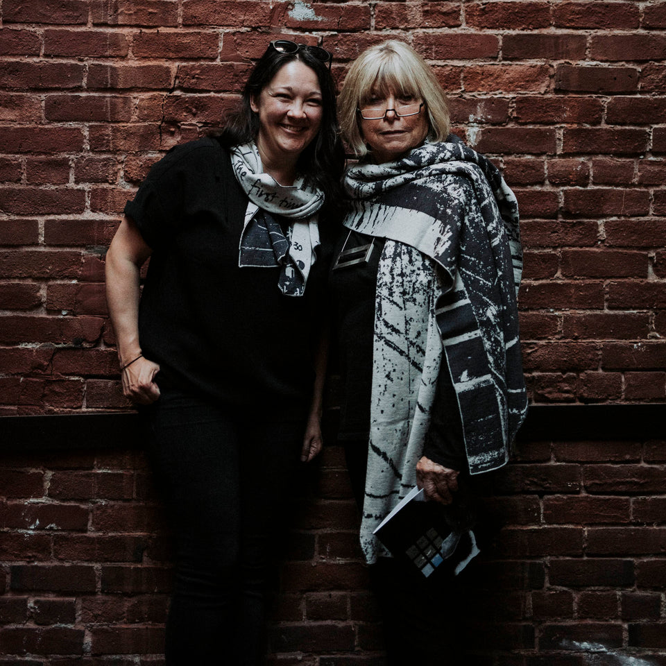 Models wear knitted Byre scarf and a knitted Byre wrap/shawl. Abstract, graphic design in an asymmetric shape. Shown in Charcoal and stone white