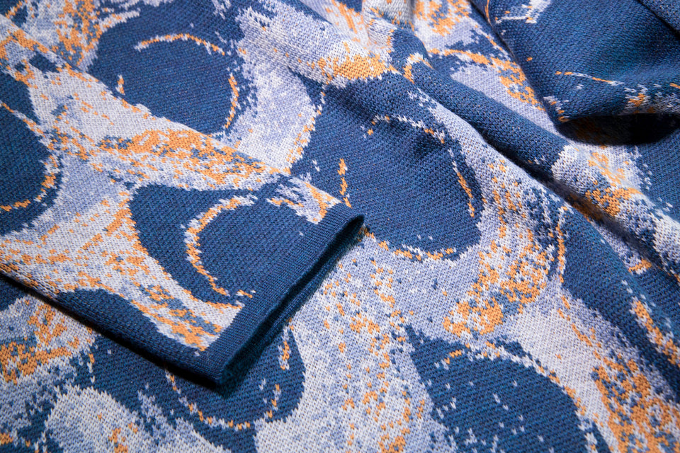 closeup up finely knitted Hoswick Paint jacket - curvilinear motifs in shaded blues with orange highlights
