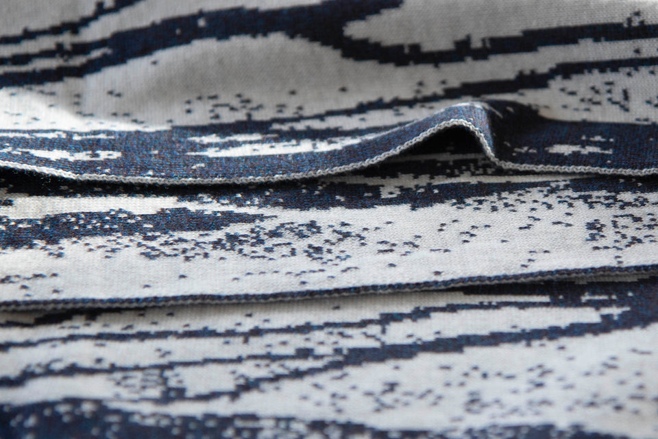 close up view of shoormal scarf showing the speckled and finely knitted fabric and the smoky blue yarn - a marl - against the off white.