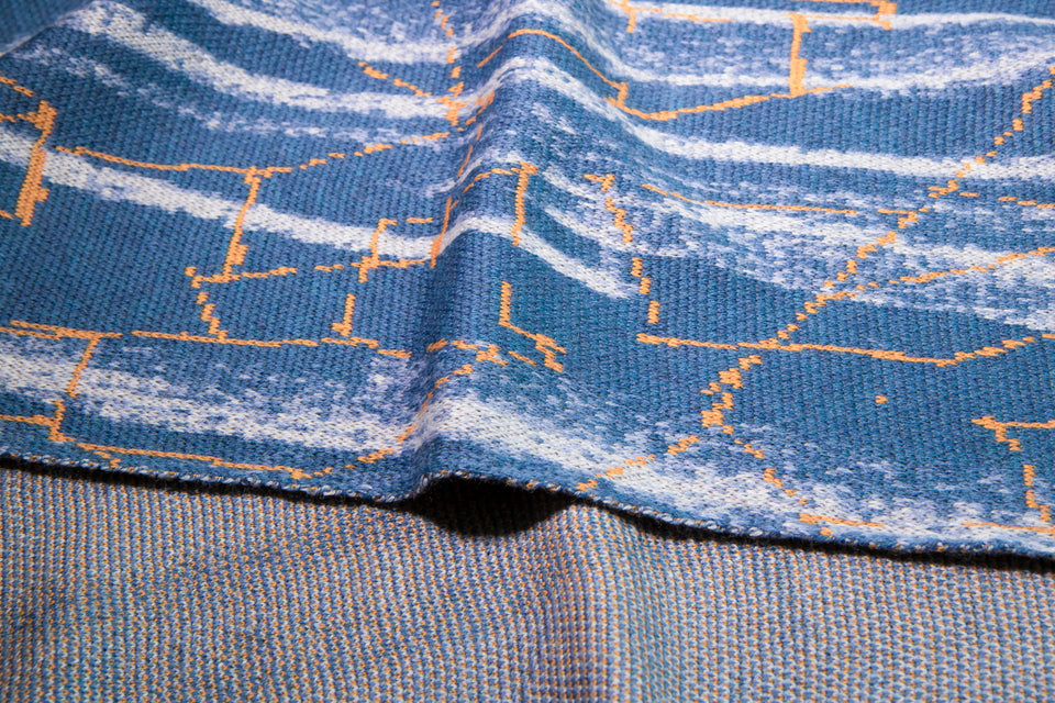 close up of scarf in blues with highlight linear patterning in orange. reverse speckle pattern also shwon.